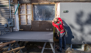 A person outside on a patio doing work on their house's insulation.