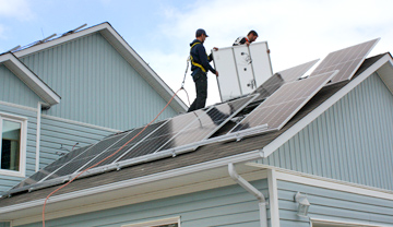2 construction workers installing solar panels on a house roof
