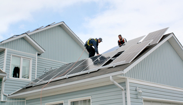 2 tradespeople installing solar panels on a  house roof.