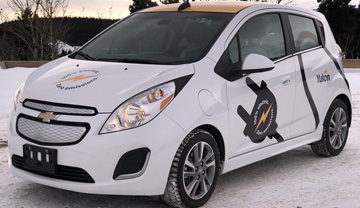 Electric car on snow covered road with sun setting